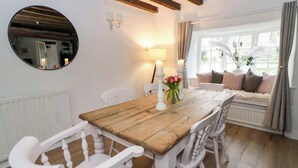 A dining area with a wooden table, white chairs, a mirror, wall sconces, and a window with curtains. - The Old Shop (Builth Wells)