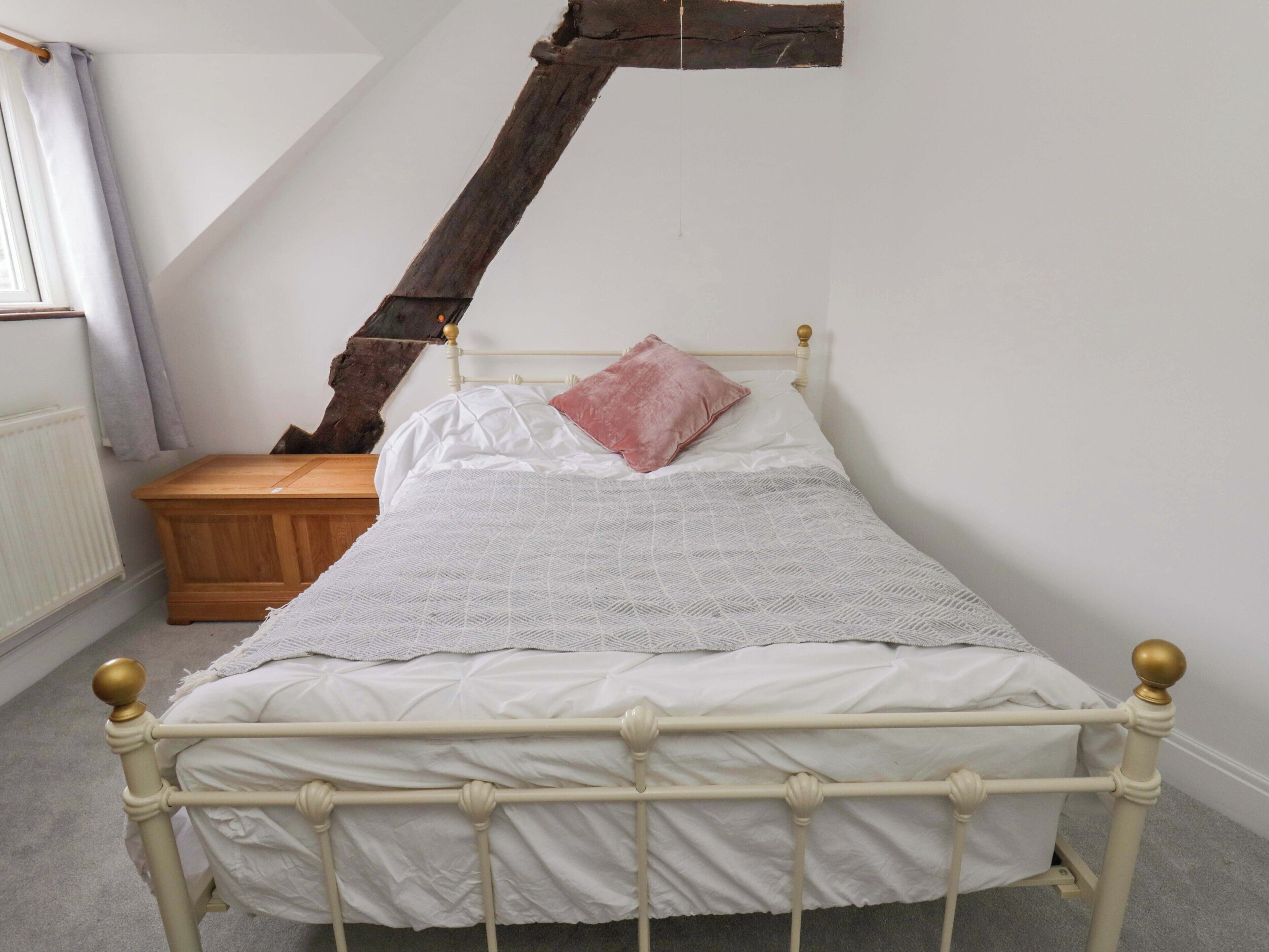 A white metal bed with a wooden headboard, a wooden nightstand, and a large window with curtains.