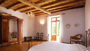 Una habitación con una cama, vigas de madera en el techo, una araña, un armario de madera y una ventana con cortinas.