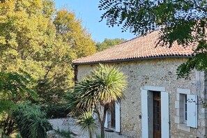 Un bâtiment en pierre avec un toit en tuiles, des volets blancs et une porte.