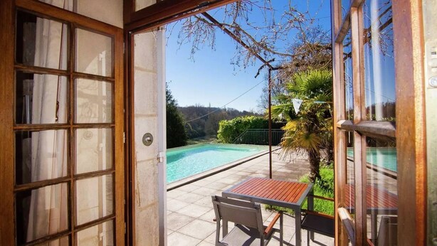 Puerta abierta que da a un patio con piscina, mesa y sillas.