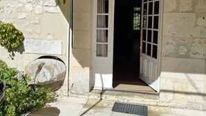 Un edificio de piedra con una puerta blanca, un pequeño escalón que lleva a la entrada y una rejilla metálica en el suelo.