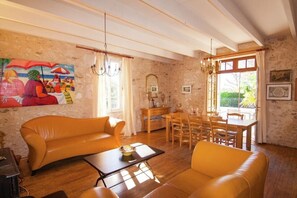 Une pièce comprenant un canapé, une table à manger, des chaises, un lustre, un tableau et un mur en pierre.