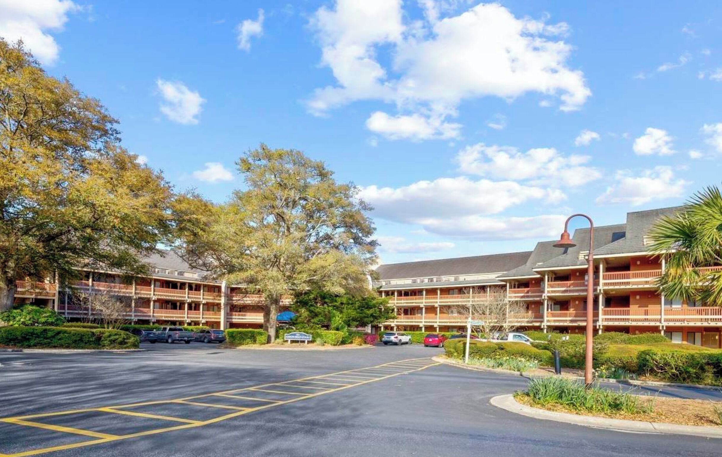 A hotel with multiple balconies, a parking lot, and surrounding trees.