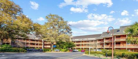 A hotel with multiple balconies, a parking lot, and surrounding trees.