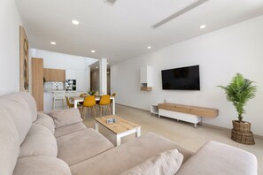 A modern living room with a sofa, a coffee table, a TV, and a dining area with chairs and a table. - Casa Manuel by Escape Home (Playa Blanca)