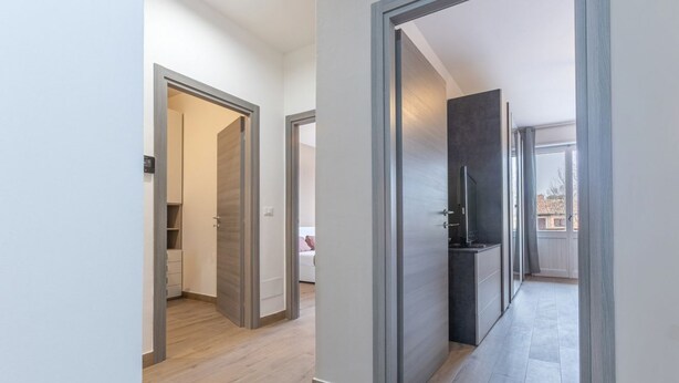 Ein Flur mit Holzboden, ein Küchenbereich mit dunkler Arbeitsplatte und ein Blick auf einen Balkon.