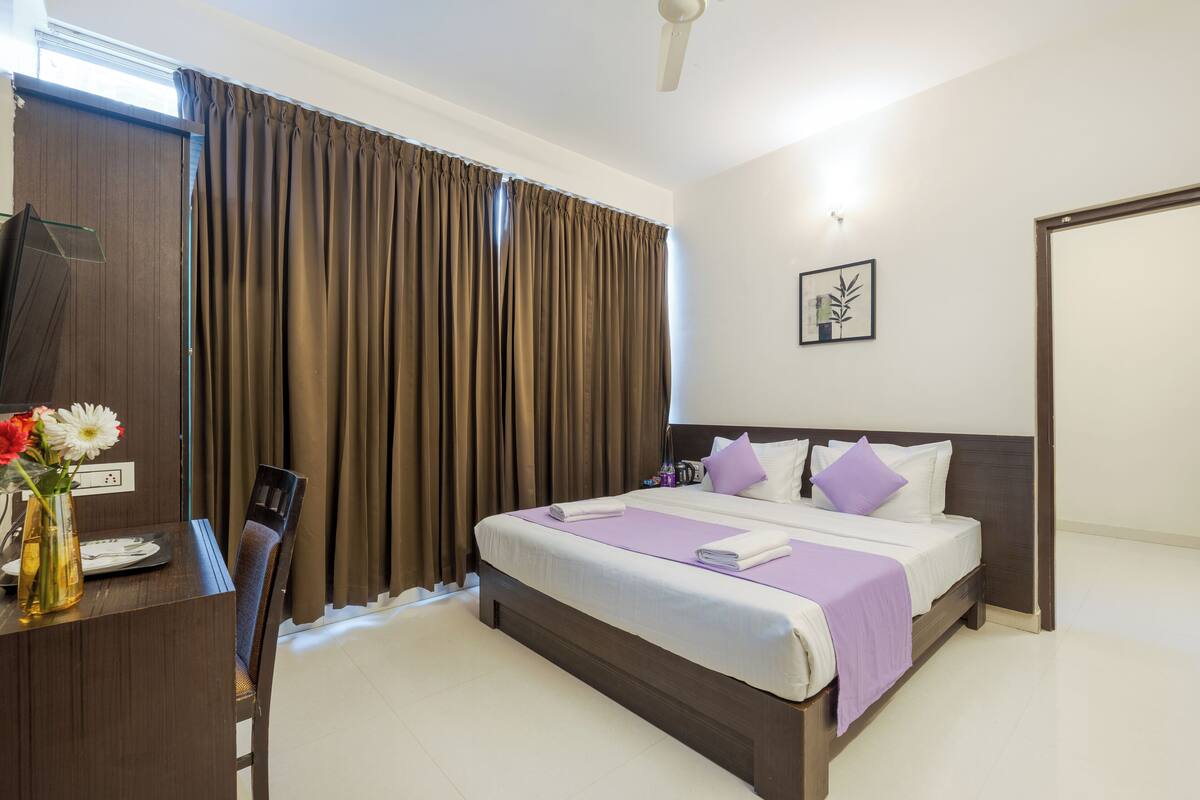 A hotel room with a bed, a desk with a vase of flowers, and a television.
