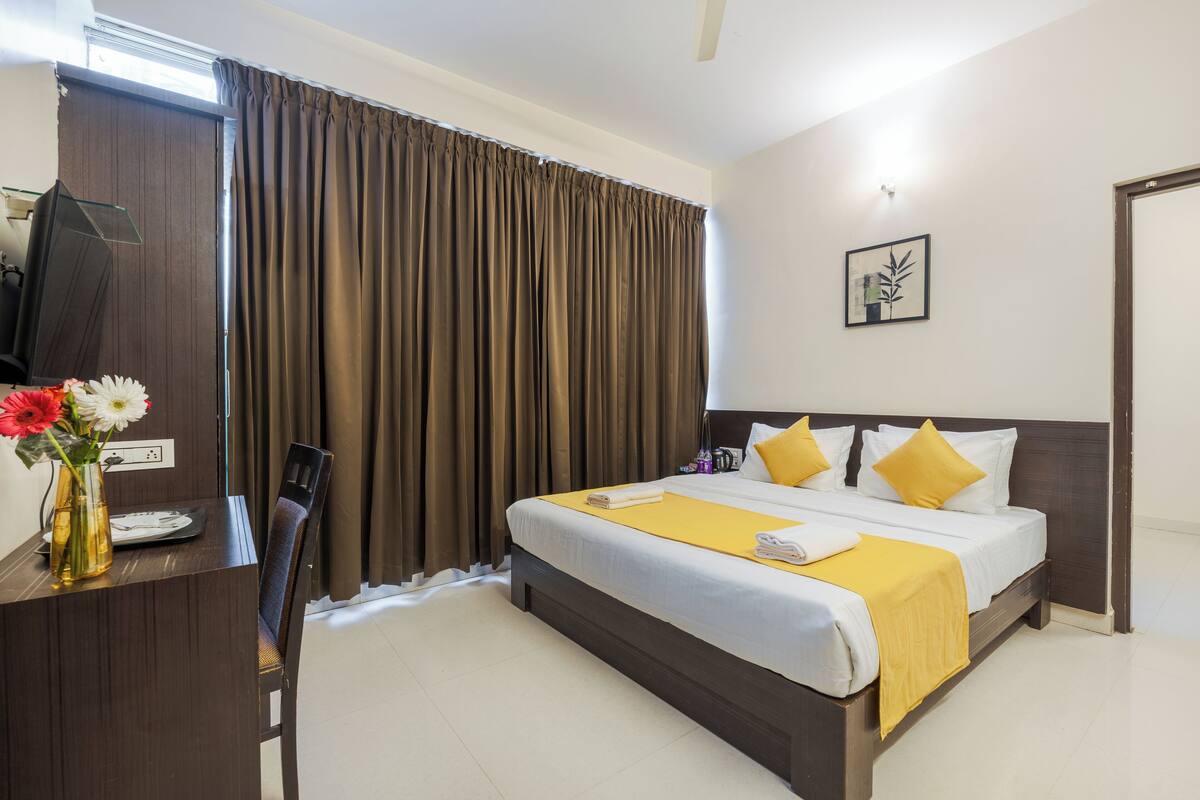 A hotel room with a bed, a desk with a chair, a TV, and a vase with flowers.