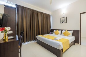 A hotel room with a bed, a desk with a chair, a TV, and a vase with flowers. - HOTEL NDS COMFORTS (Bengaluru)
