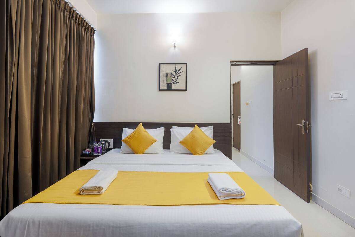 A hotel room with a bed, a nightstand, a door, and a wall-mounted light.