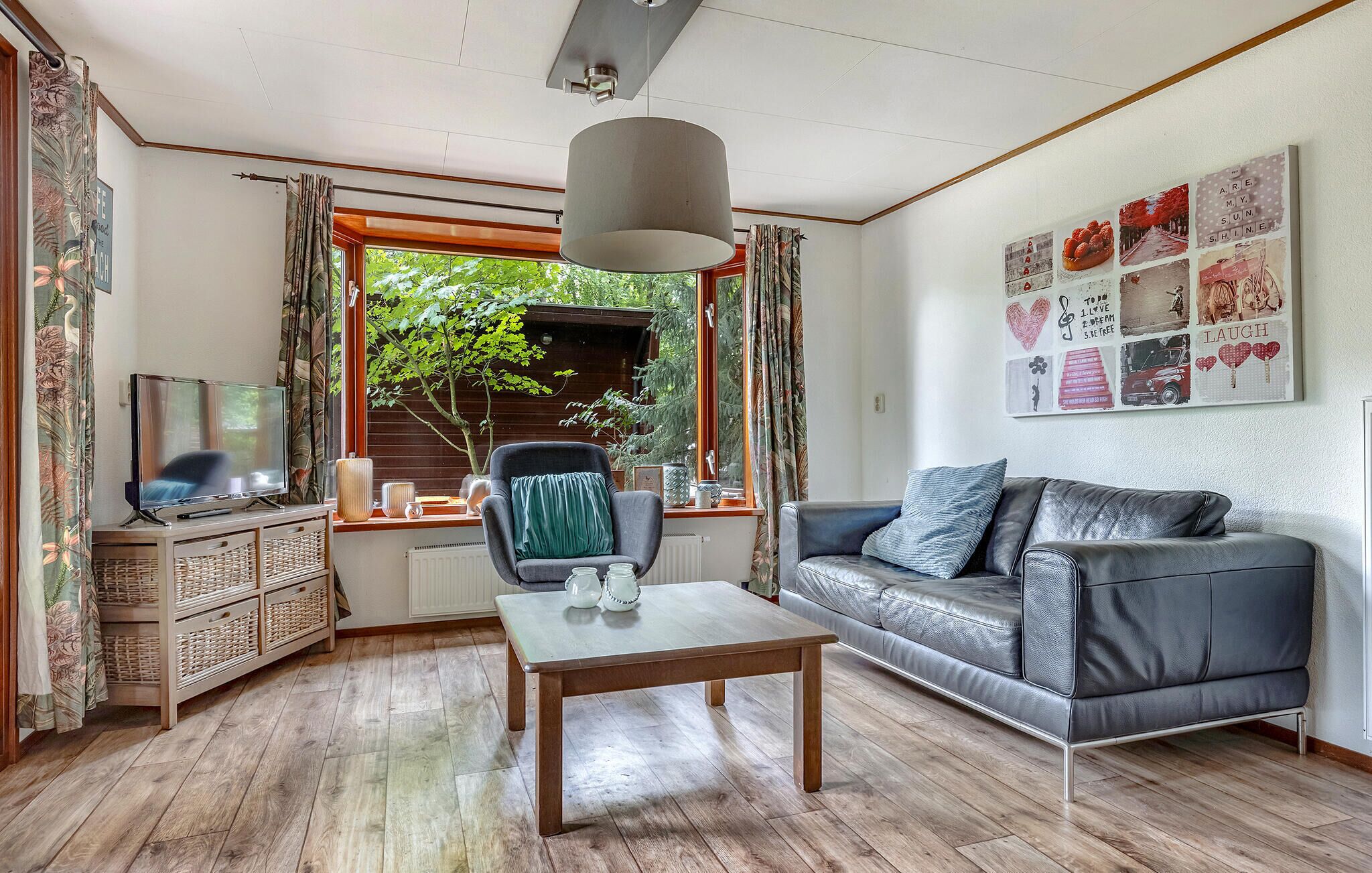 Ein Wohnzimmer mit Holzboden, einer Couch, einem Tisch, einem Fernseher und einem Fenster mit Vorhängen.