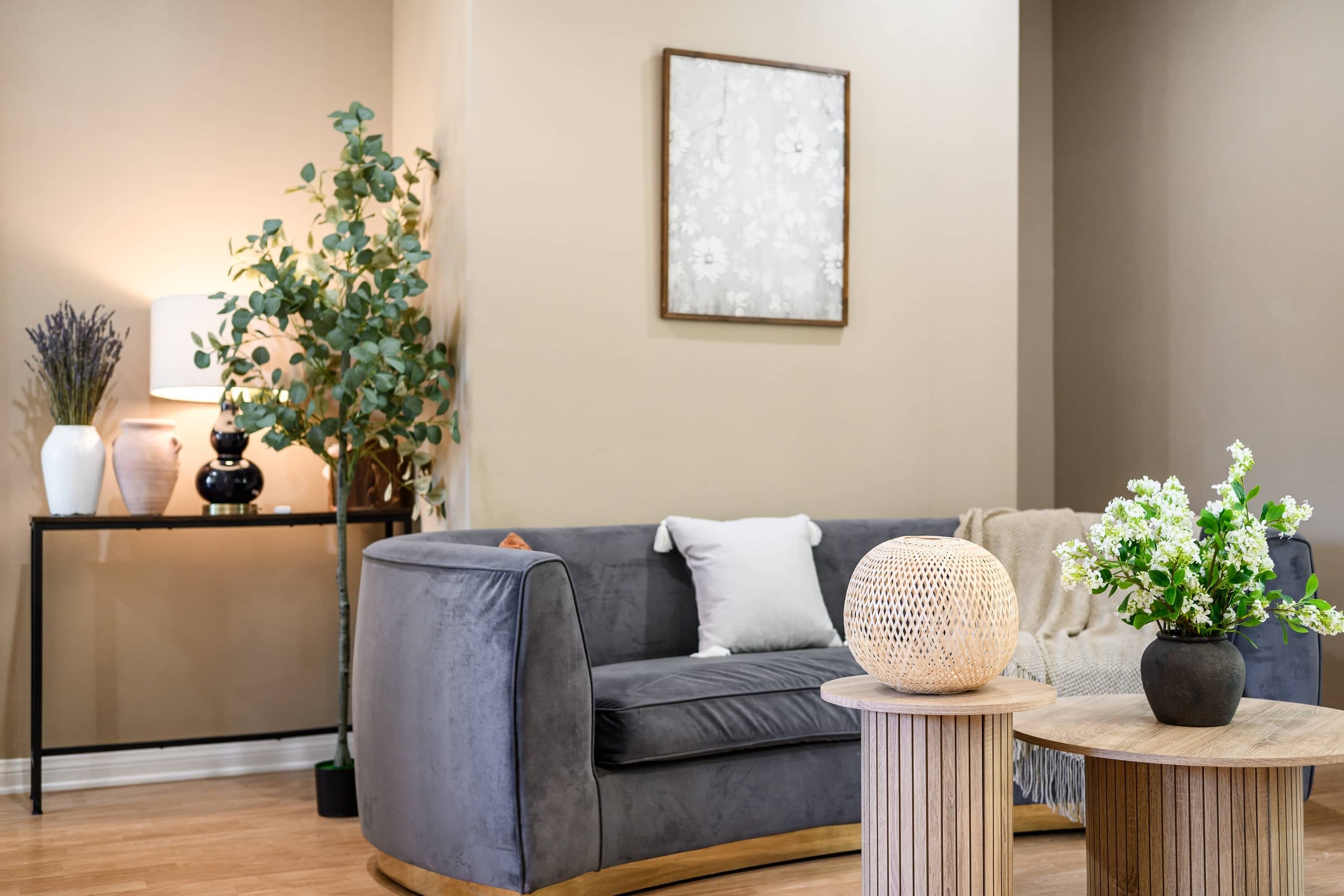 A modern living room with a grey sofa, a round wooden coffee table, a side table with a lamp, and a potted plant.
