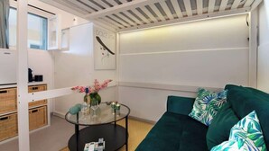 Een moderne woonkamer met een groene bank, een glazen salontafel, rieten manden en een wandplank.
