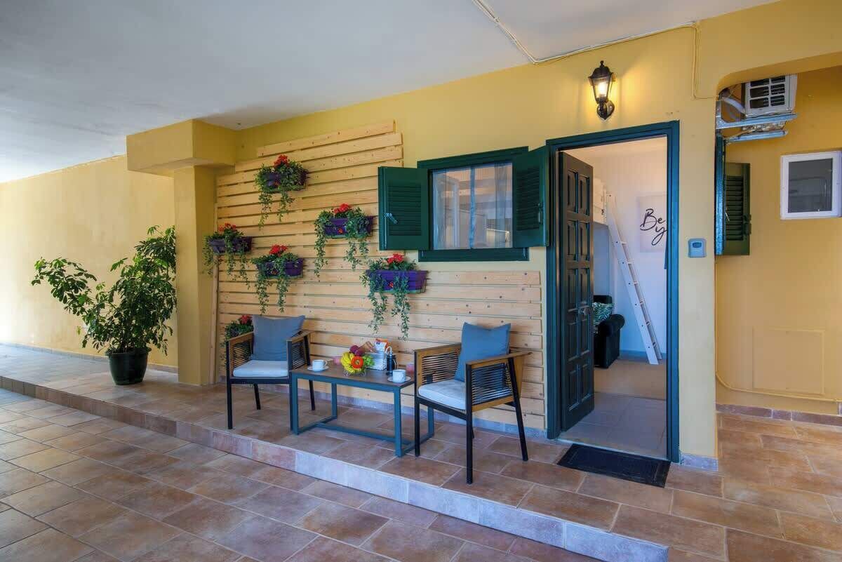 A covered outdoor seating area with a wooden wall, green shutters, and potted plants.