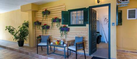 A covered outdoor seating area with a wooden wall, green shutters, and potted plants.