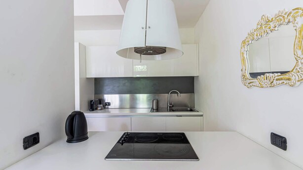 Een moderne keuken met witte kasten, een roestvrijstalen afzuigkap, een zwart inductiekookveld, een gootsteen met een kraan, en een decoratieve spiegel met gouden lijst.