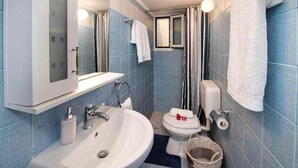 A compact bathroom with a white sink, toilet, and shower area. - Fenia s Studio - Charming Getaway in Gaios Paxos (Paxos)