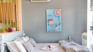 A neatly made bed with pillows and a folded towel, a wall-mounted artwork, and a window with a view of the outdoors. - Fenia s Studio - Charming Getaway in Gaios Paxos (Paxos)