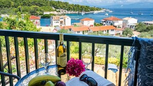 A balcony with a table set for a meal, overlooking a coastal village with boats and houses. - Fenia s Studio - Charming Getaway in Gaios Paxos (Paxos)