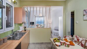 A compact kitchen with a view of the sea, a dining area with a table set for two, and a sofa with a floral pattern. - Fenia s Studio - Charming Getaway in Gaios Paxos (Paxos)