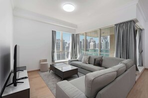 A modern living room with a grey sofa, a coffee table, and a TV on a stand. Large windows offer a view of a cityscape. - A Free Housekeeping Visit FOR Every Stay Between THE 16th FEB AND THE 16th MAR - Stayshort - Spacious 2 Bedroom in Dubai Marina That Sleeps 6 (Dubai)