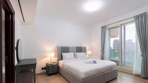 Ein modernes Hotelzimmer mit einem großen Bett, Nachttischlampen, einem kleinen Schreibtisch und Blick auf die Stadt durch große Fenster.