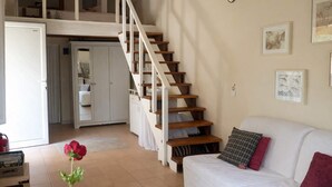 Un vaste espace de vie avec un canapé blanc, un escalier en bois et une cuisine en arrière-plan.