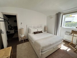 Un dormitorio con una cama grande, una mesita de noche, una lámpara, una silla y una ventana con cortinas.
