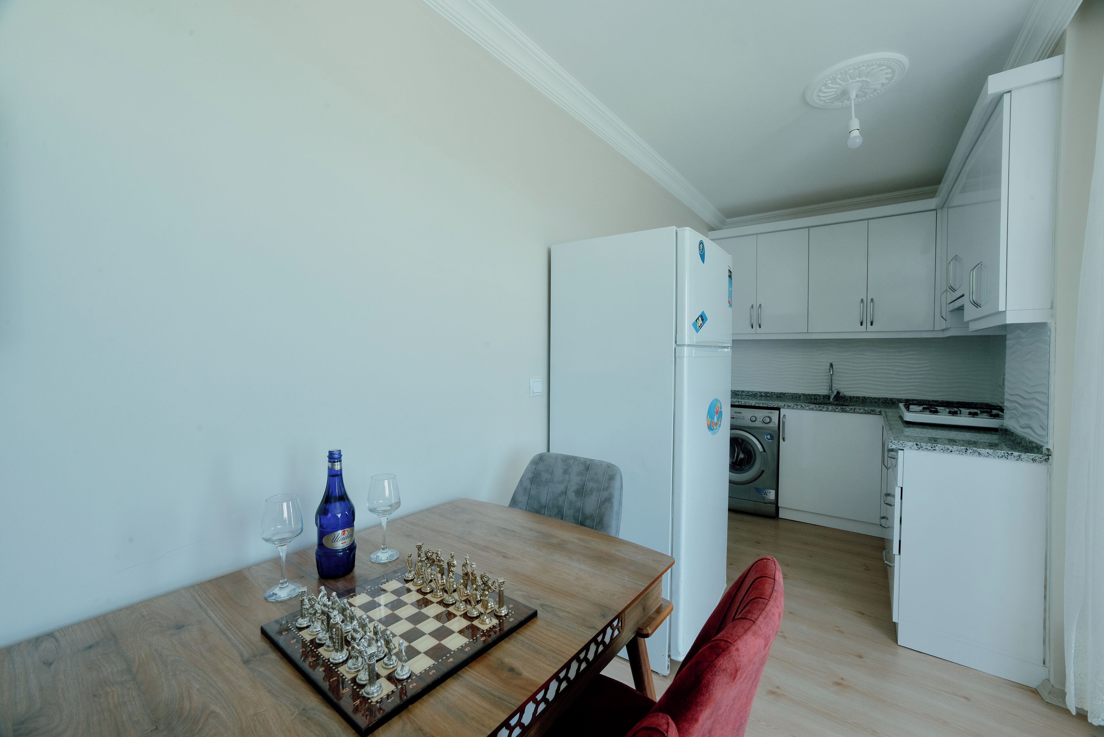 A compact kitchen with a dining area, a washing machine, and a chessboard on the table.