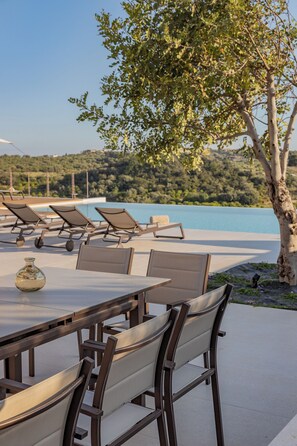 A terrace with a table and chairs, overlooking a body of water and a hilly landscape. - Altamira Luxury Villa with pool in Noto (Noto)