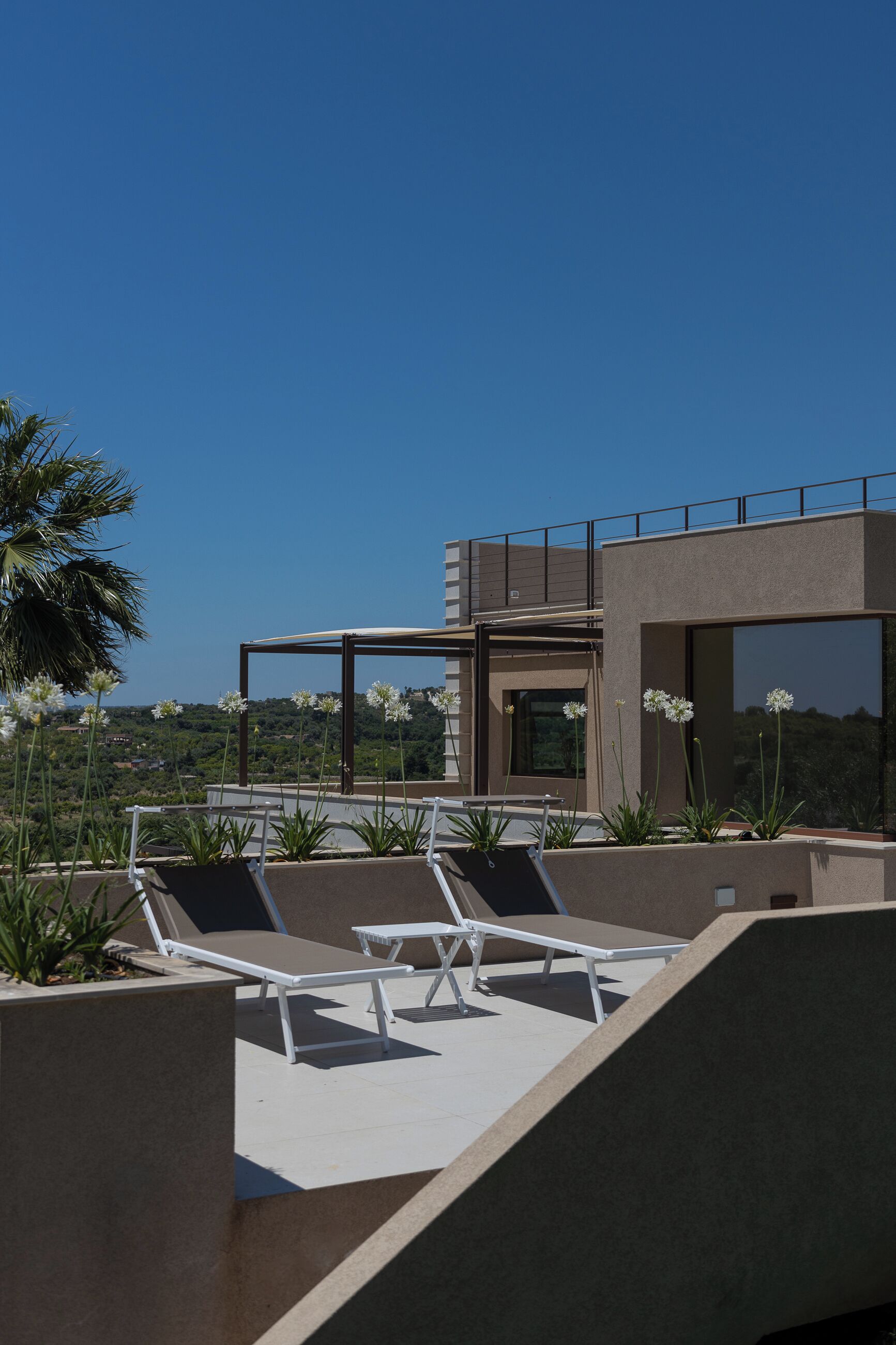 A rooftop terrace with lounge chairs, a pergola, and a view of the landscape.
