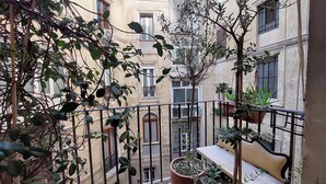Een balkon met een bankje, bloempotten en uitzicht op omliggende gebouwen.