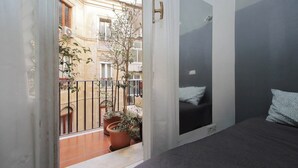 Een kamer met een bed, een deur naar een balkon en uitzicht op een gebouw met balkons en plantenpotten.