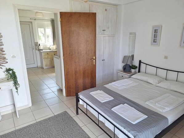 A bedroom with a bed, bedside tables, a wardrobe, and a bathroom visible in the background. - Horizon studio apartments (Lefkada)