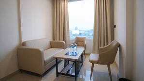 Une chambre d’hôtel avec un canapé, un fauteuil, une petite table et une fenêtre avec des rideaux.