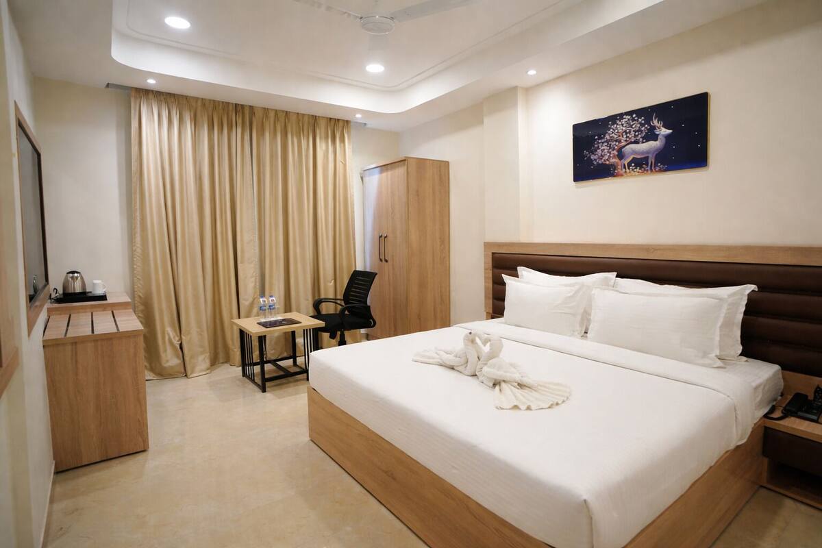 A hotel room with a bed, a desk, a chair, a wardrobe, and a painting on the wall.
