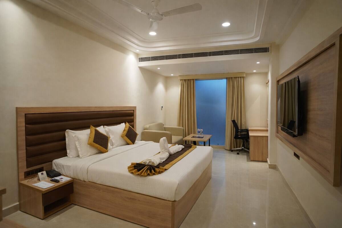 A hotel room with a large bed, a desk, a chair, a TV, and a balcony with curtains.