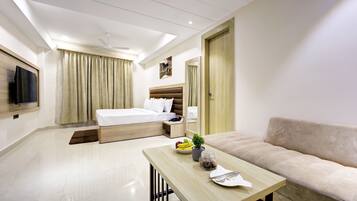 Habitación de hotel con cama, sofá, mesa con planta y frutero, televisión y ventilador de techo.