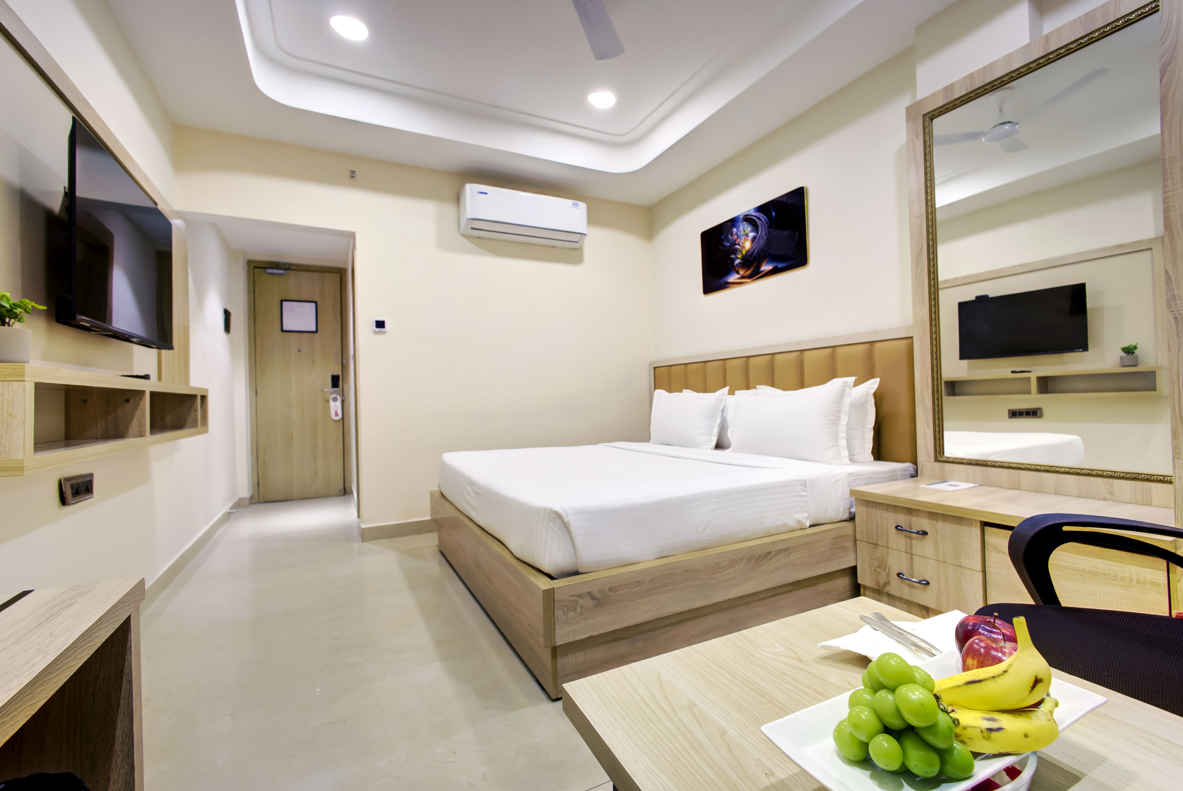 A hotel room with a bed, bedside table, desk, chair, and a flat-screen TV.