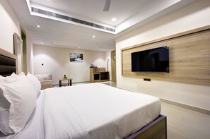 A hotel room with a bed, a TV mounted on the wall, a desk, and a chair. - Cozzet Royale (Kanpur)