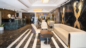 Un hall d’hôtel moderne avec un comptoir d’accueil, un espace salon et un grand lustre.