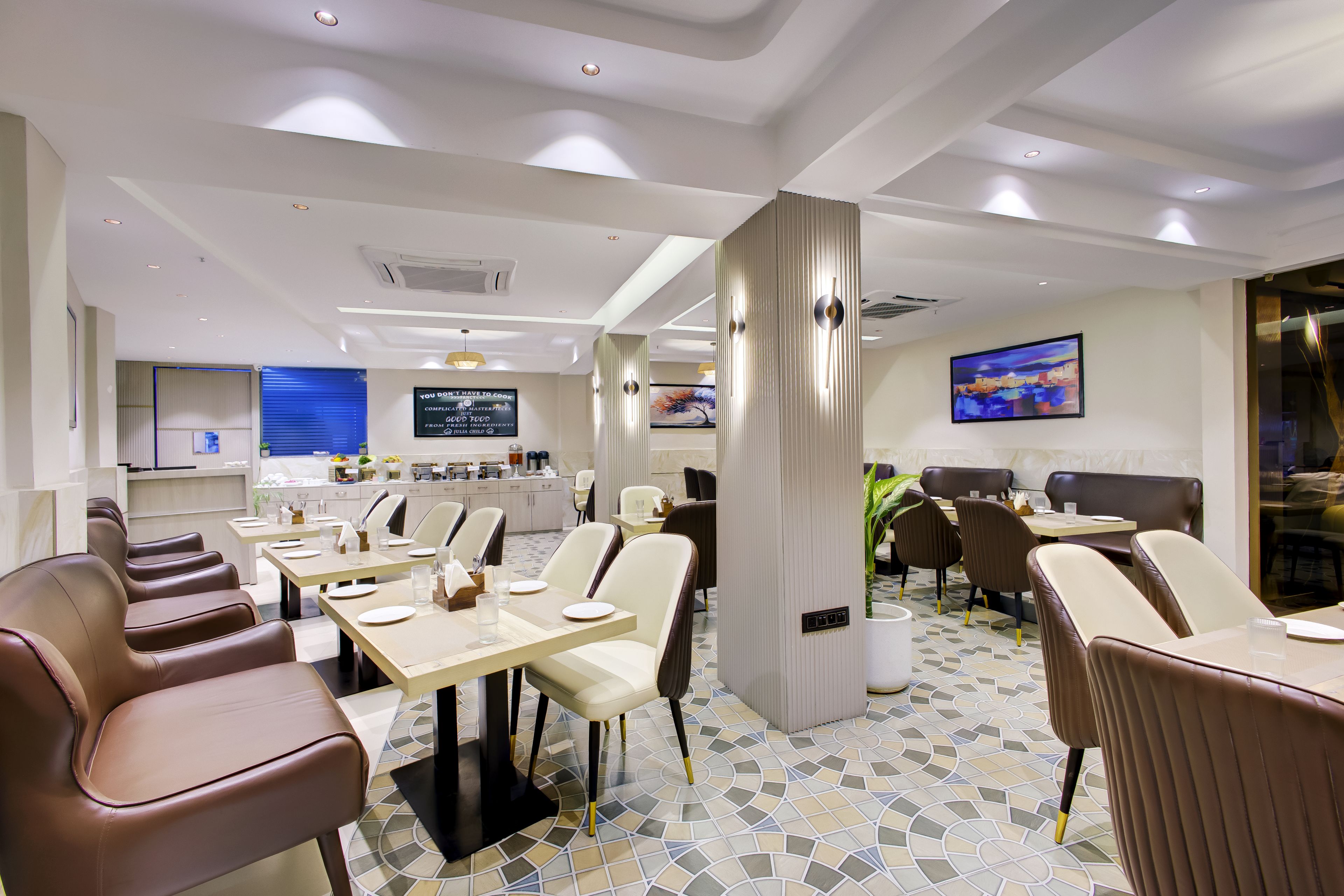 A modern restaurant interior with multiple dining tables and chairs, a kitchen area in the background, and a large painting on the wall.