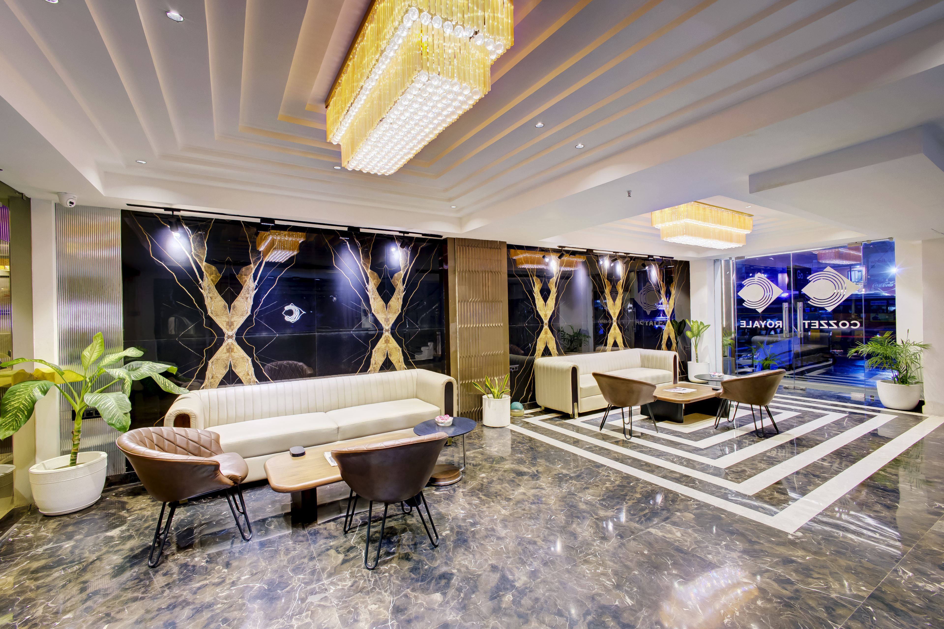 A modern lobby with a seating area, a large chandelier, and a glass wall with a reflection of a Coca-Cola sign.