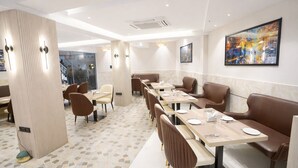 Un restaurant moderne avec des banquettes et des tables, un sol carrelé et un grand tableau abstrait accroché au mur.