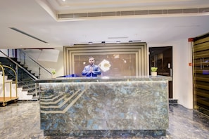 A reception desk with a marble top, a staircase to the left, and a closed shutter to the right. - Cozzet Royale (Kanpur)