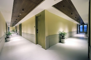 A corridor with a wooden ceiling, green doors, and potted plants. - Cozzet Royale (Kanpur)