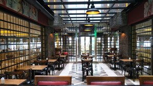 Interior de restaurante con paredes de ladrillo, mesas de madera y lámparas colgantes.