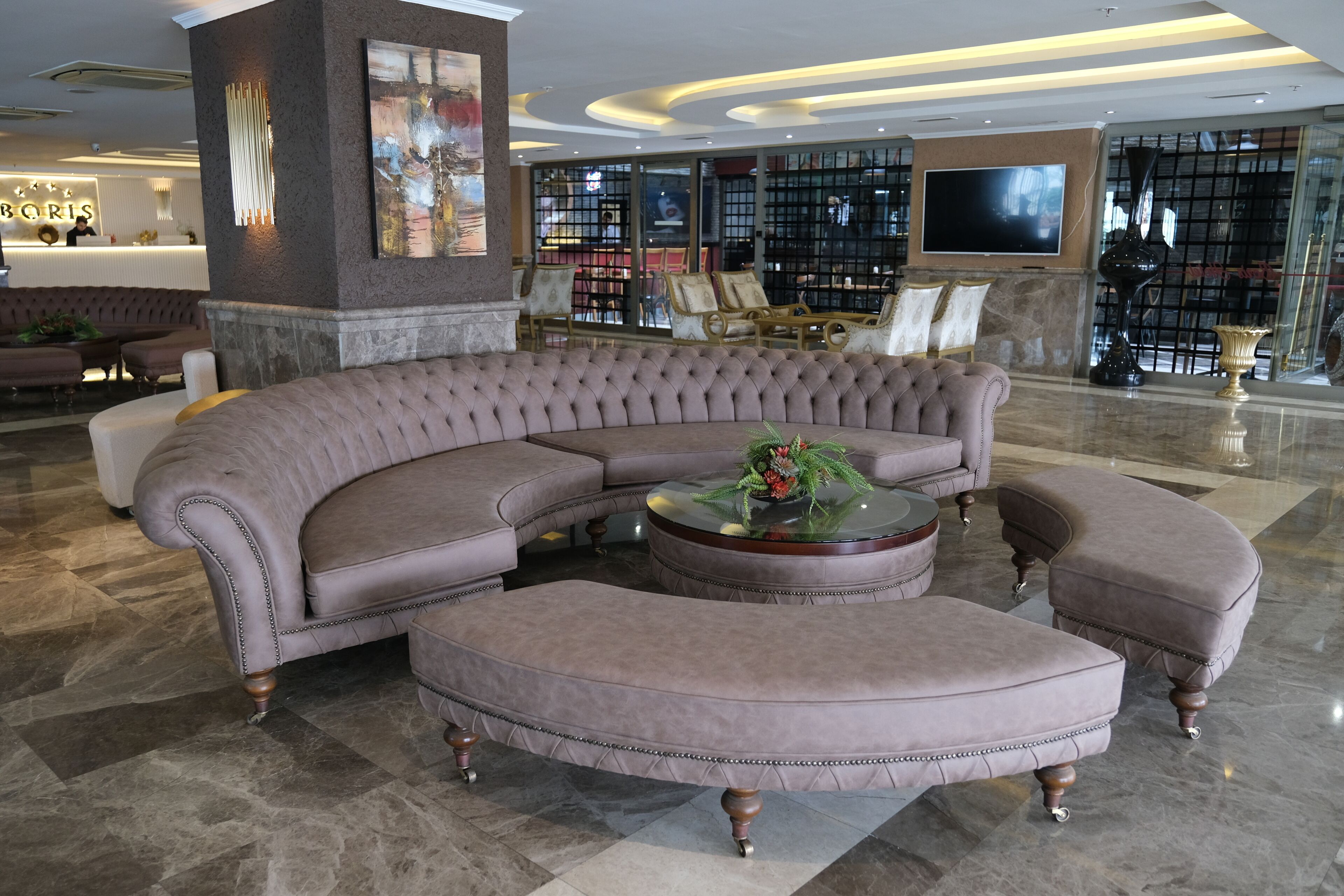Eine moderne Lobby mit einer großen Eckcouch, einem runden Couchtisch und einer Rezeption.
