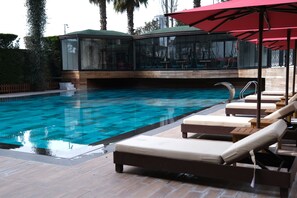 A swimming pool with lounge chairs and umbrellas, a glass-enclosed area with seating, and a wooden deck. - BORİS OTEL  (İstanbul)